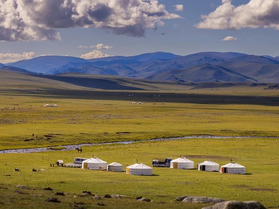 Ger camp beside a river on the Mongolian steppe, with mountains beyond